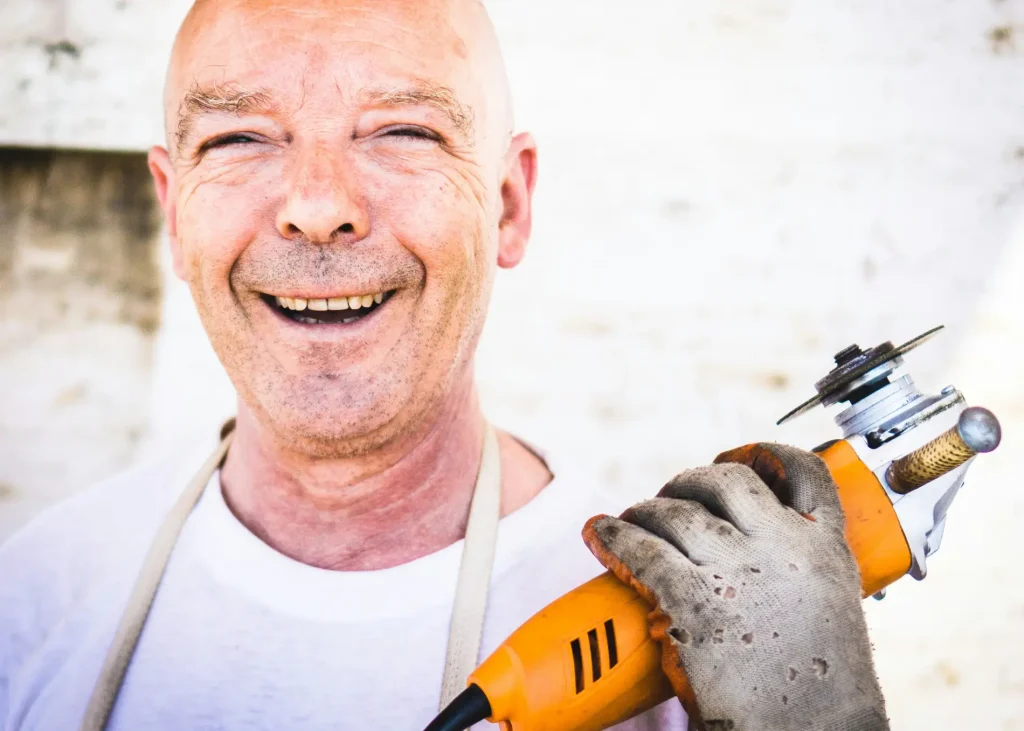 a man smiling, holding a power tool, gratitude