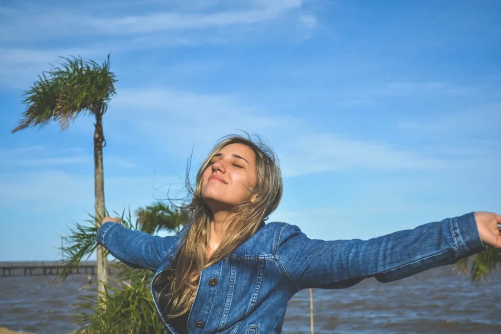 girl standing near palm trees and the sea, with her arms stretched out and she is happy