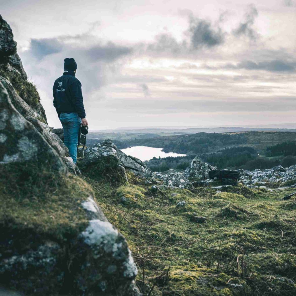 A man standing on a rock looking out over the moors towards some water.