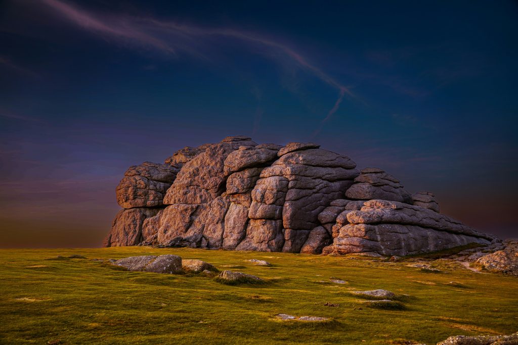 dartmoor tor with a dark sky and bright sunlingt hitting the rock face