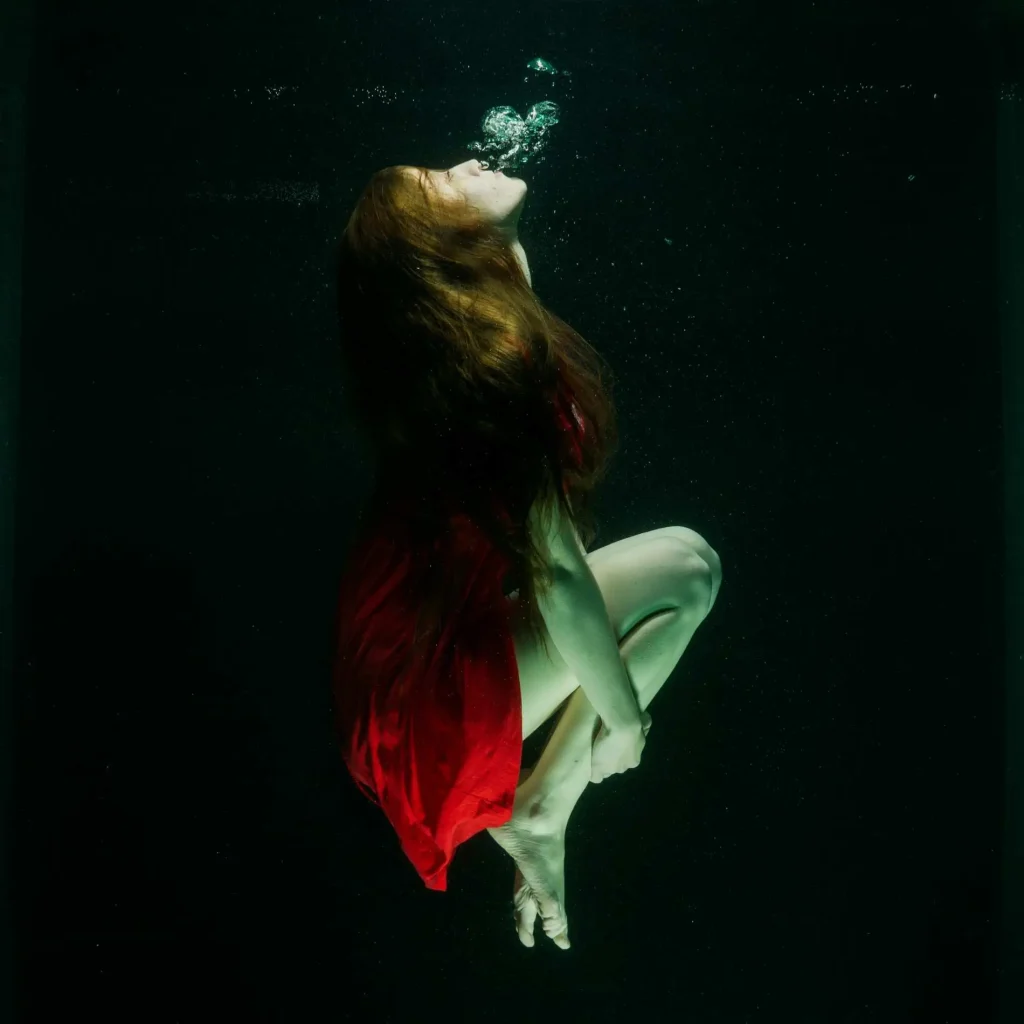 a woman submerged underwater breathing out, meditating, shadow work, breathwork