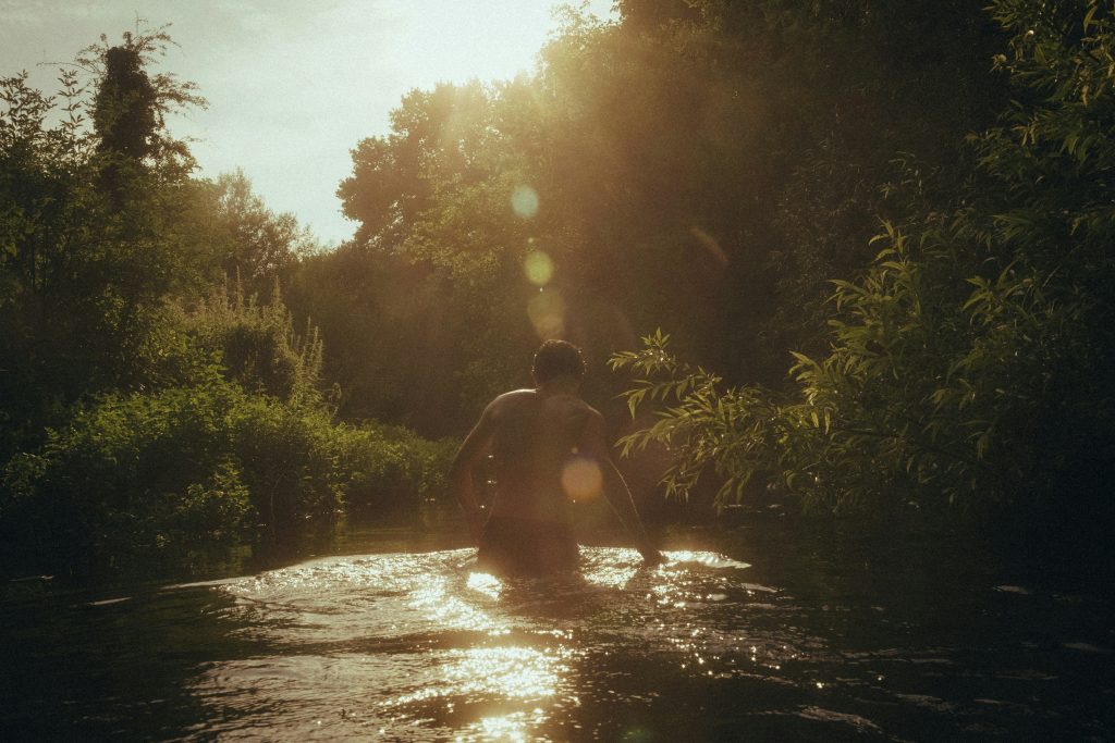 a man in the river with the sun shining down and some green trees